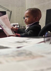 a young boy in a suit reading a newspaper