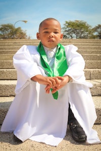 a young boy in a white robe sitting on a set of steps