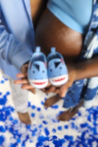 a pregnant woman holding a pair of blue baby shoes